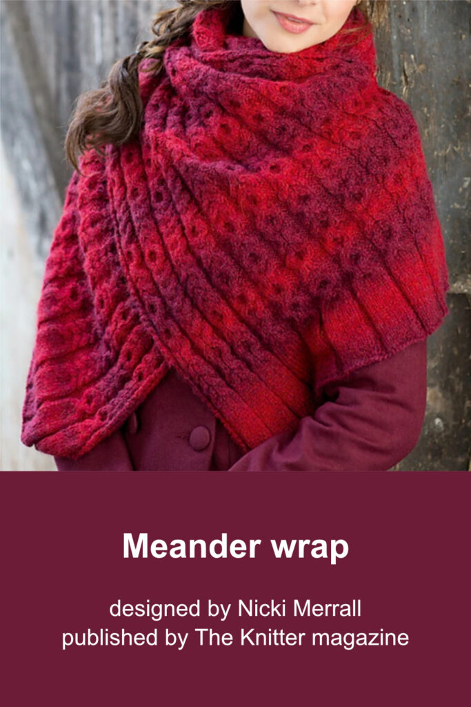 Woman wearing large cable wrap in a variegated red and burgundy yarn