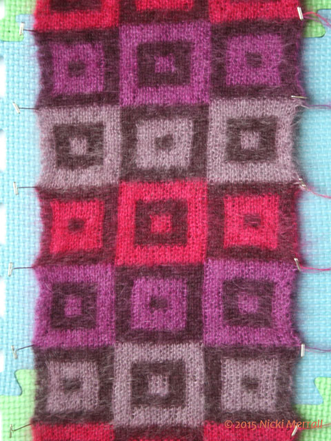 A piece of knitting with a grid design pinned to blocking boards
