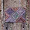 Photo of Kairouan greetings card on wooden background. Greetings card shows detail of hand-knit throw worked in mitred squares using variegated yarns