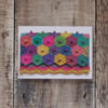 Photo of Magic of the Circus greetings card on a wooden background. Greetings card shows a knitted clutch bag: the flap features mitred hexagons and the main part has chevrons