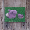 Photo of Bunnies greetings card on wooden background. Greetings card shows two small grey knitted bunnies sitting on grass