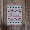 Photo of Noel greetings card on wooden background. Greetings card shows chart for Fair Isle or cross stitch design featuring fir trees, holly and the word Noel