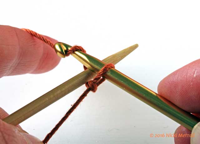 Pass crochet hook over knitting needle and grab yarn with hook