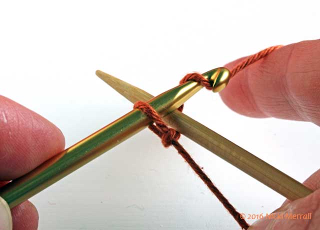 Pass crochet hook over knitting needle and grab yarn with hook