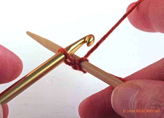 Pass yarn backwards between hook and needle