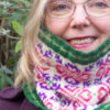 Close-up of woman wearing Fair Isle style cowl with pink and purple large allover motif on white background and green ribs