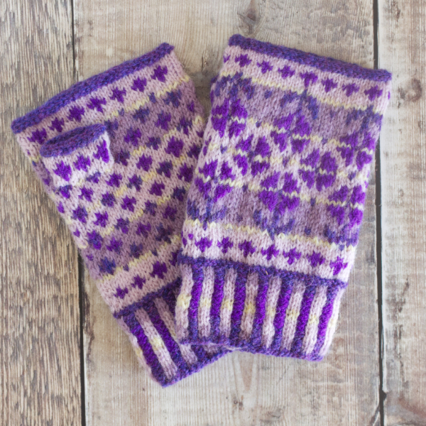 Hand-knitted Fair Isle style fingerless mitens with corrugated rib, a simple peerie pattern and a large pattern featuring flowers. Worked in violet and purple on a lilac, mauve and pale yellow background.