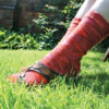 Hand-knitted socks in a red variegated yarn worn by model is sitting in sunny garden