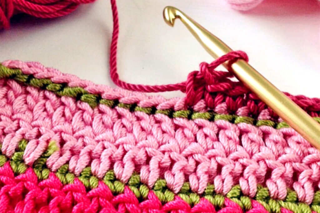 Pink and green crochet sample on a hook showing basic crochet stitches.