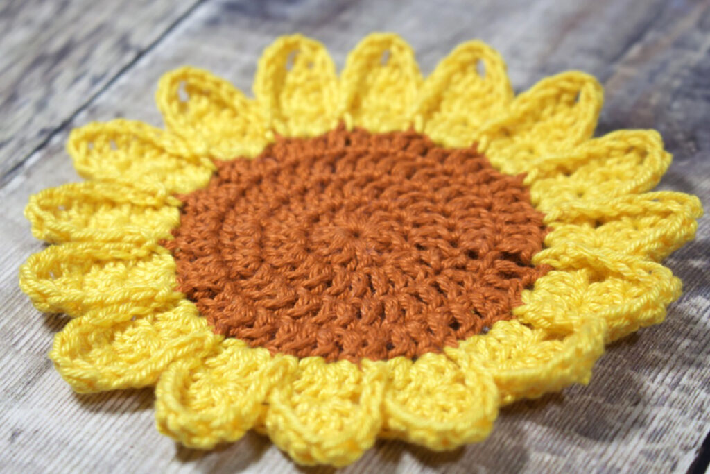 A large crochet sunflower with golden yellow petals and a bright brown centre.